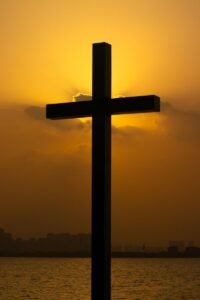 a cross is silhouetted against a sunset over a body of water